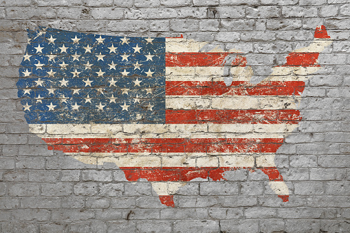 Grunge distressed map shaped flag of USA painted on old weathered grey brick wall
