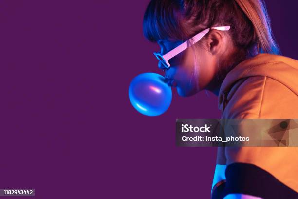 Teen Igen Girl Wear Stylish Trendy Sunglasses And Hoodie Blowing Bubble Gum Profile Side View Pretty Young Woman Fashion Cool Model With Bubblegum 80s At Party Purple Studio Background Copy Space Stock Photo - Download Image Now