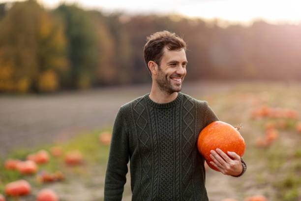Man holding pumpkin in pumpkin patch field