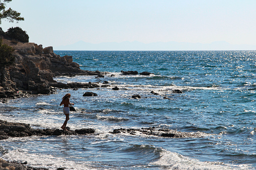 Woman alone at the rocky beach looking over the horizon with wavy sea on a wind day in Mediterranean