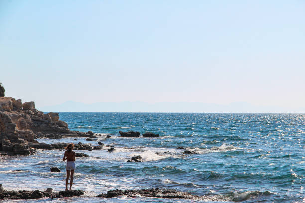 Woman alone at the rocky beach looking over the horizon with wavy sea on a wind day in Mediterranean