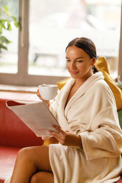 mujer sonriente leyendo revista mientras bebe té en el spa. - tea women beauty pampering fotografías e imágenes de stock