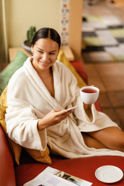 istock Happy woman drinking tea while using phone at the spa. 1182950598