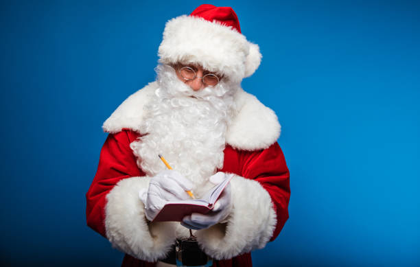 istock Taking notes. Authentic Santa Claus is posing with a notebook in his left hand, where he writes with the pen, which he holds in his right hand. 1182958260