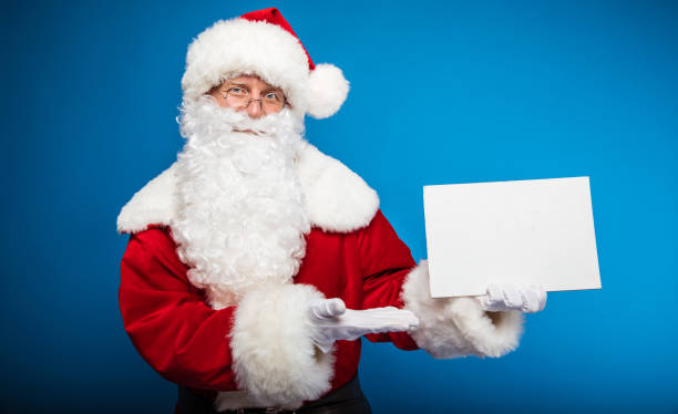 istock Look! Real Santa is pointing with his right hand at the blank postcard with copyspace on it, which he holds in his left hand, looking at the camera calmly. 1182958552