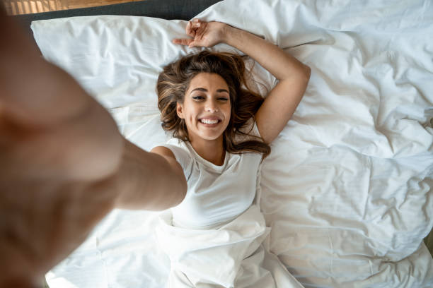 piękna kobieta leżąca na łóżku i robiąca selfie - lying in bed zdjęcia i obrazy z banku zdjęć