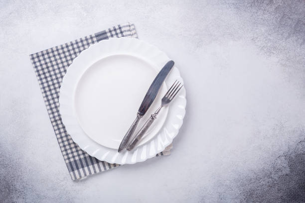 istock Empty white plate, linen napkin, knife and fork on stone background Copy space Top view 1182964832