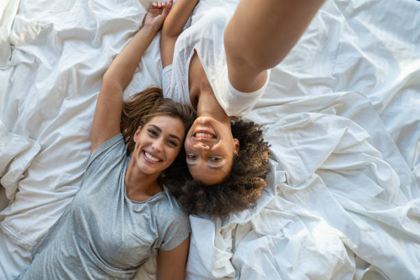 istock Two female friends lying on bad and taking selfie 1182965473