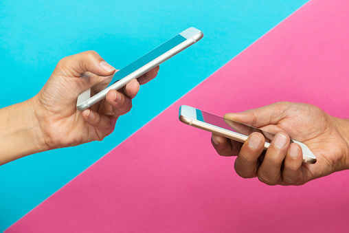 Man and woman holding smart phones on blue and pink background.