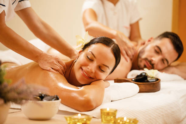 Happy couple enjoying a day at spa while having back massage. Young couple enjoying in back massage at health spa. Focus is on smiling woman. massage therapist photos stock pictures, royalty-free photos & images