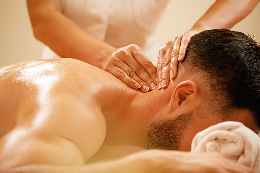 Close-up of therapist massaging man's neck during spa treatment.