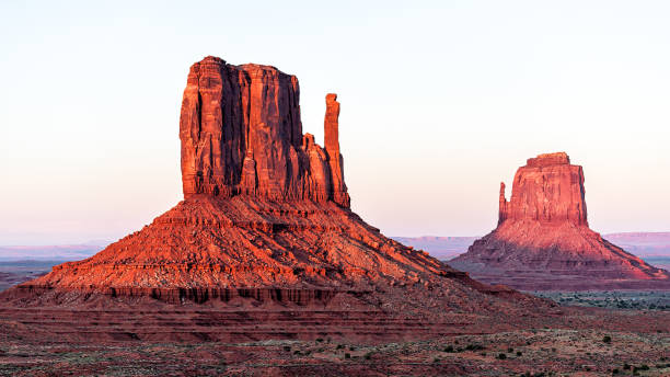 panoramic view of two mittens butte mesa with colorful red orange rock color on horizon in monument valley canyons during sunset in arizona - merrick butte imagens e fotografias de stock