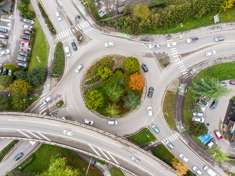 Roundabout road intersection with vehicle traffic and green trees aerial view from drone showing circular shape and lanes, transportation junction architecture