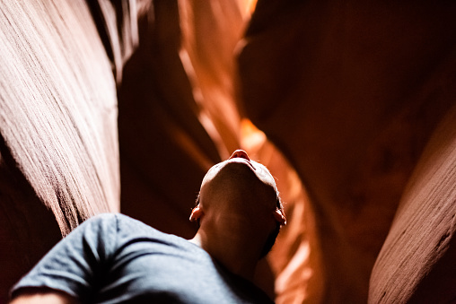 Low angle view of young man inside Upper Antelope slot canyon in Arizona looking up at dark rock sandstone wave shape formations