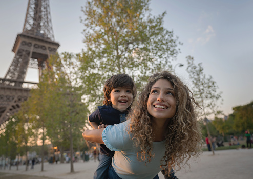 Portrait of two very happy tourists sightseeing in Paris and mother carrying son on a piggyback ride near the Eiffel Tower