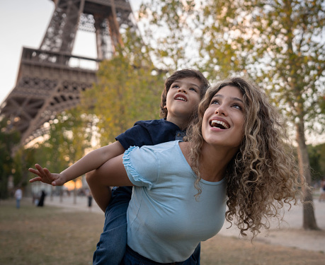 Excited mother and son sightseeing in Paris carrying her son on a piggyback ride