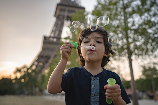 Portrait of a happy boy playing around making bubbles in Paris with the Eiffel Tower at the background