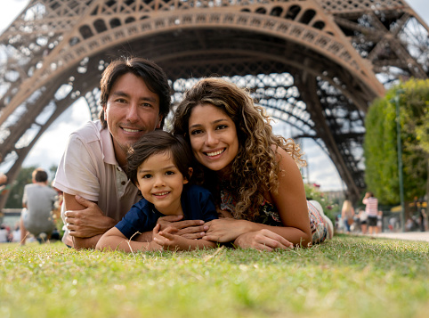 Portrait of a happy family in Paris relaxing at the park with the Eiffel Tower at the background and looking at the camera smiling