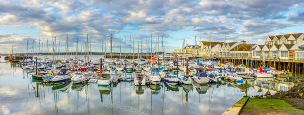 Marina and harbor in Southampton, UK, with tranquil waters reflecting clouds, sky.