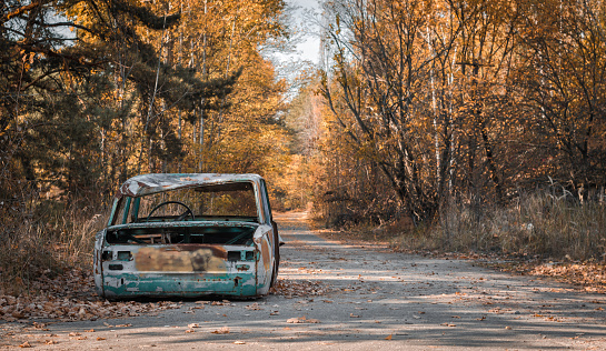 road with a broken car with trees and fallen leaves in Chernobyl Ukraine in autumn