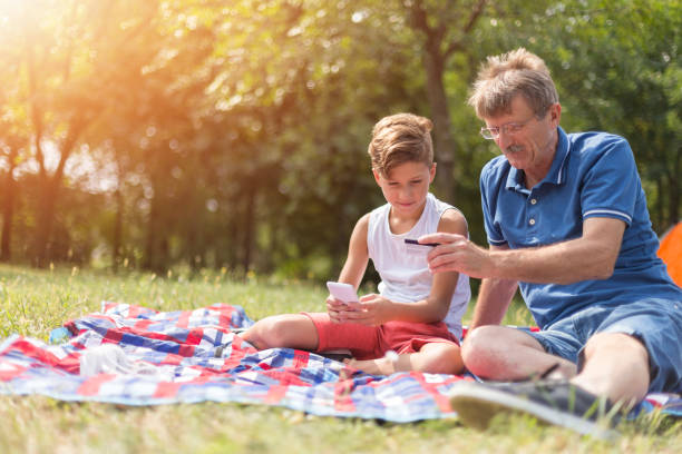 Boy and senior man online shopping while resting in nature