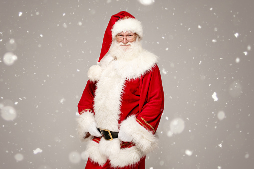 Real Santa Claus in red cap posing on grey studio background. Merry Christmas and Happy New Year concept.