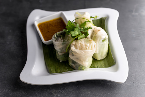 Shrimp Udang Roll with basil, bean sprouts, and peanut dipping sauce. Plated with a banana leaf, on a slate table.