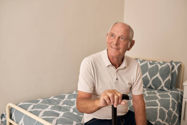 istock Smiling senior man sitting with a cane on his bed 1182998312