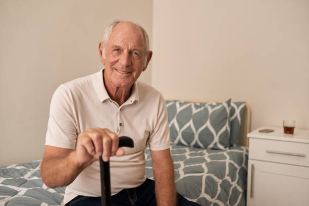 istock Smiling senior man sitting on his bed holding a cane 1182998410