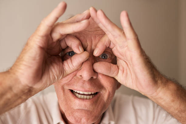 lächelnder senior, der durch die fingerbrille schaut - human hand old senior adult aging process stock-fotos und bilder