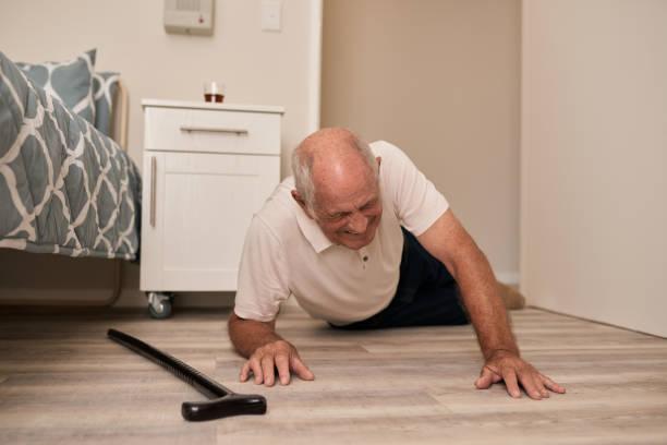 Senior man grimacing in pain after a fall Senior man wincing in pain beside his walking cane after falling on the floor of his room in an assisted living home grimacing photos stock pictures, royalty-free photos & images