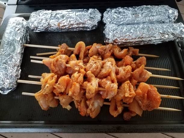 istock raw chicken on wood sticks and corn wrapped in foil on grill 1183021307