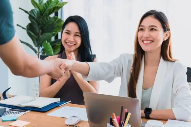 Beautiful young Asian girl and businesswoman meeting & shake hands at a office space with a laptop on table. Concept of female leader working business success.