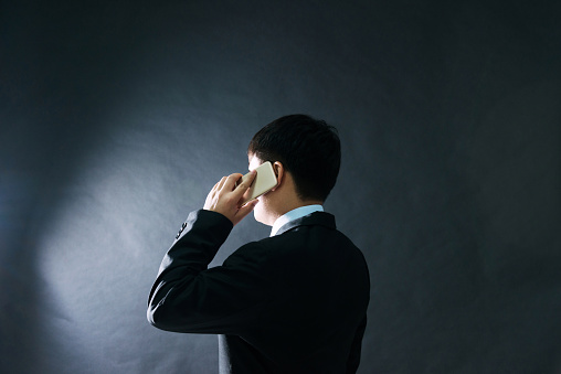 Rear view of businessman using phone on black background.