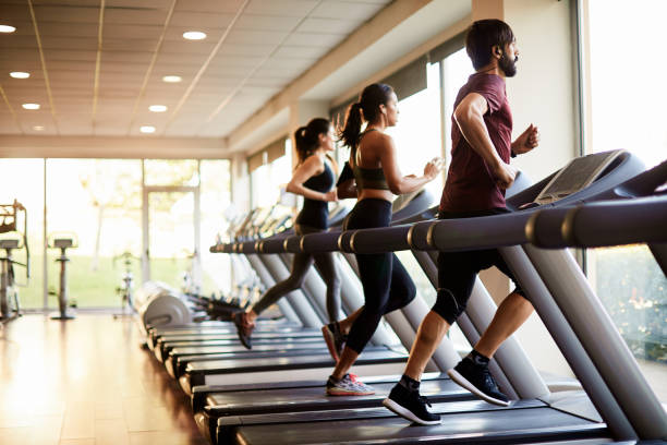 blick auf eine reihe von laufbändern in einem fitnessstudio mit menschen. - adult jogging running motivation stock-fotos und bilder