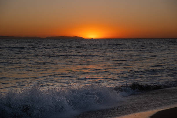 The last moments of sun reflect off the water in Newport Beach, California. A trail of footprints in the sand are about to be erased by the rising tides.