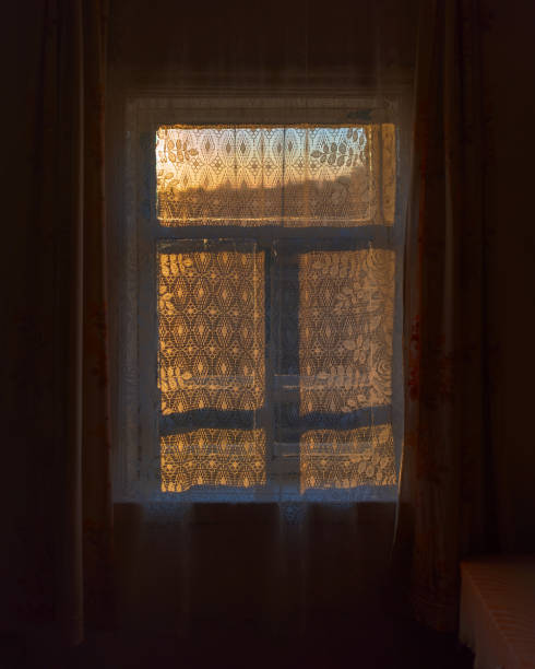 istock A dark, rustic room with a corner table and a window behind a curtain with the setting sun at sunset. 1183039947