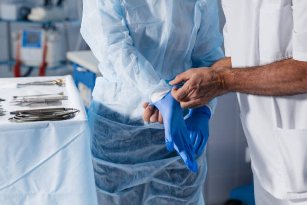 Assistant helping surgeon to put on latex gloves while standing in surgery Unrecognizable surgical male assistant helping surgeon to put on latex gloves while standing in surgery close up. putting on latex gloves stock pictures, royalty-free photos & images