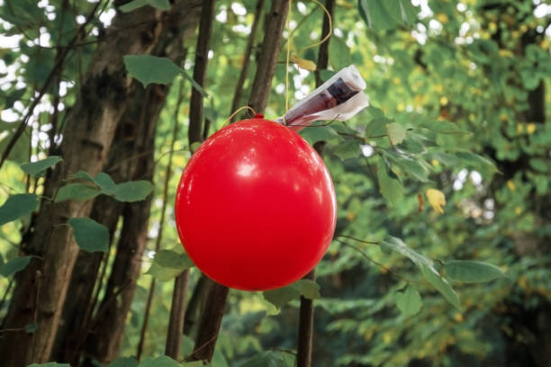 globo rojo con nota adjunta a él como parte de una caza de carroñeros o juego de rastro de papel colgando de un árbol en un bosque - scavenger hunt fotografías e imágenes de stock