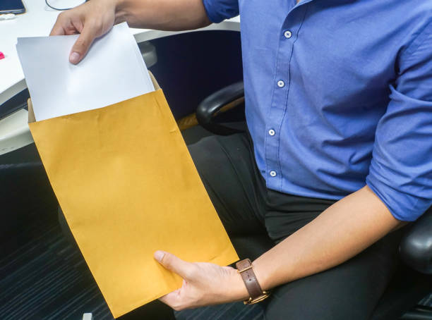 close up selective focus businessman put confidential documents into brown envelope in office stock photo