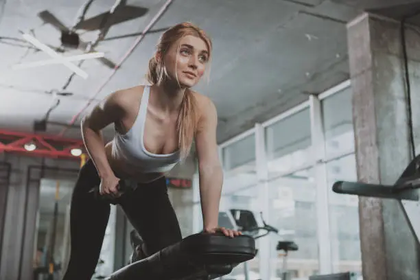 Low angle shot of a gorgeous athletic woman lifting weights at the gym, copy space. Attractive sportswoman doing back muscles workout at sport studio. Body building, lifestyle concept