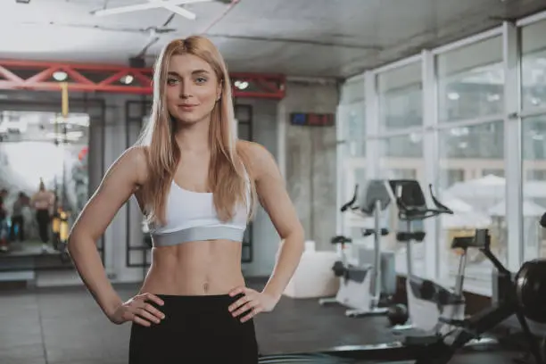 Happy healthy beautiful sportswoman smiling to the camera, standing in spacious gym, copy space. CHeerful athletic woman in sportswear preparing to workout at sport studio