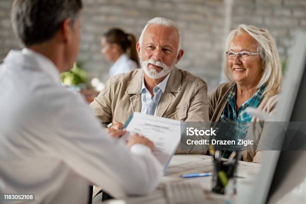 Happy Senior Couple Going Through Medical Insurance Paperwork With A Doctor Stock Photo - Download Image Now