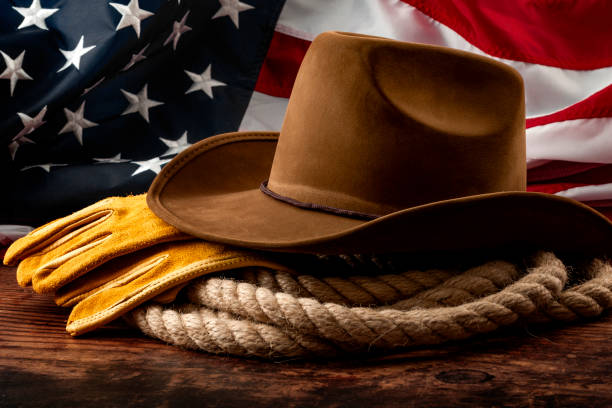 amerikanische kultur, unabhängigkeitstag in den vereinigten staaten von amerika und 4. juli konzeptthema mit cowboyhut, usa-flagge, seil-lasso und bauernhandschuhen auf holzhintergrund in einem alten salon - western theme stock-fotos und bilder