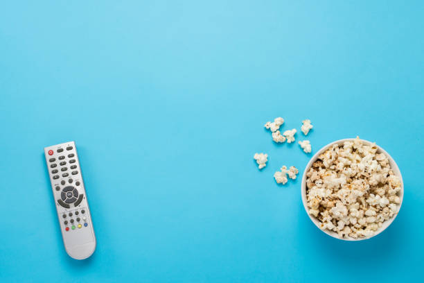 istock Bowl with popcorn and remote control for TV on a blue background 1183054932