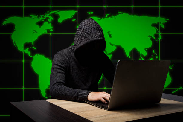 istock Faceless man in a hooded robe sits at a table with a laptop. The 1183055349