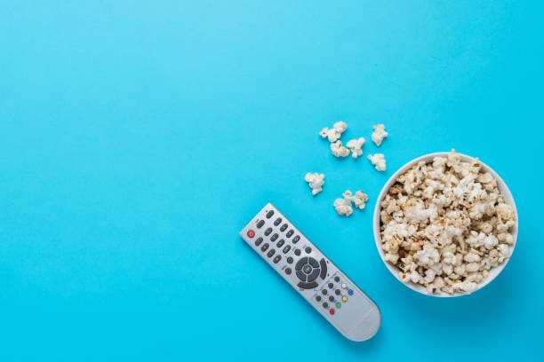 istock Bowl with popcorn and remote control for TV on a blue background 1183055490
