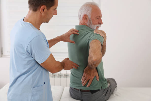 背痛的老人脊柱物理治療師和美容師。脊椎止痛緩解療法。年齡相關背痛 - 人關節 圖片 個照片及圖片檔