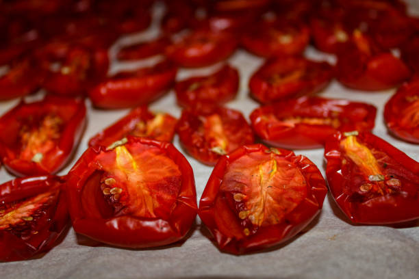 Sun-dried tomatoes. Dried, red, juicy. Close-up, blurred edges. Lie on a white parchment on a baking sheet, in even rows. Delicious Italian product. The process of making a house. Health food. Preservation. Produce.