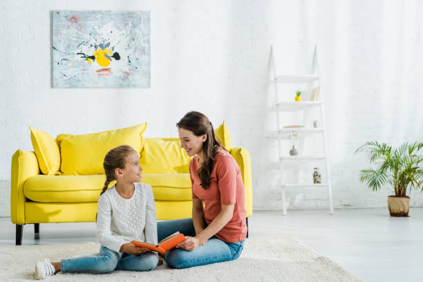 istock happy kid holding book while sitting on carpet with babysitter 1183074418